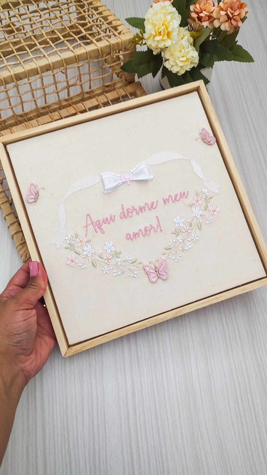Quadro bordado com flores, laço e a frase Aqui dorme meu amor